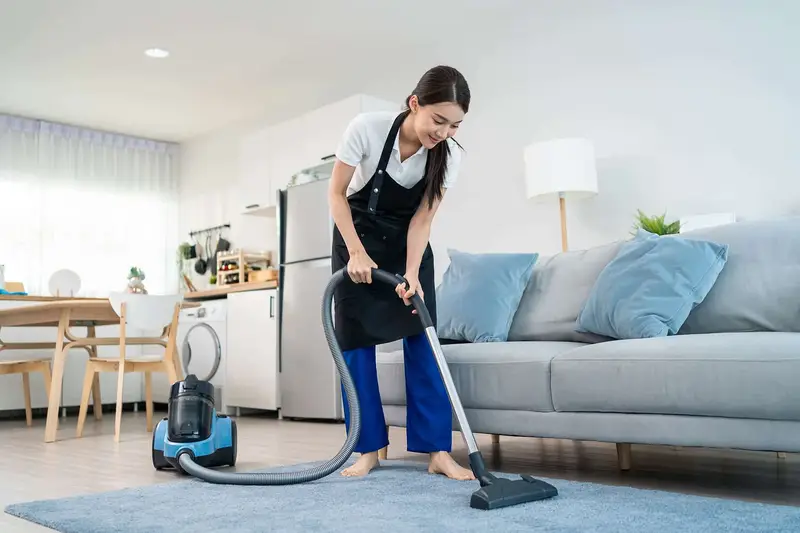 A professional cleaner wiping a kitchen counter or vacuuming a living room in a bright, tidy home.